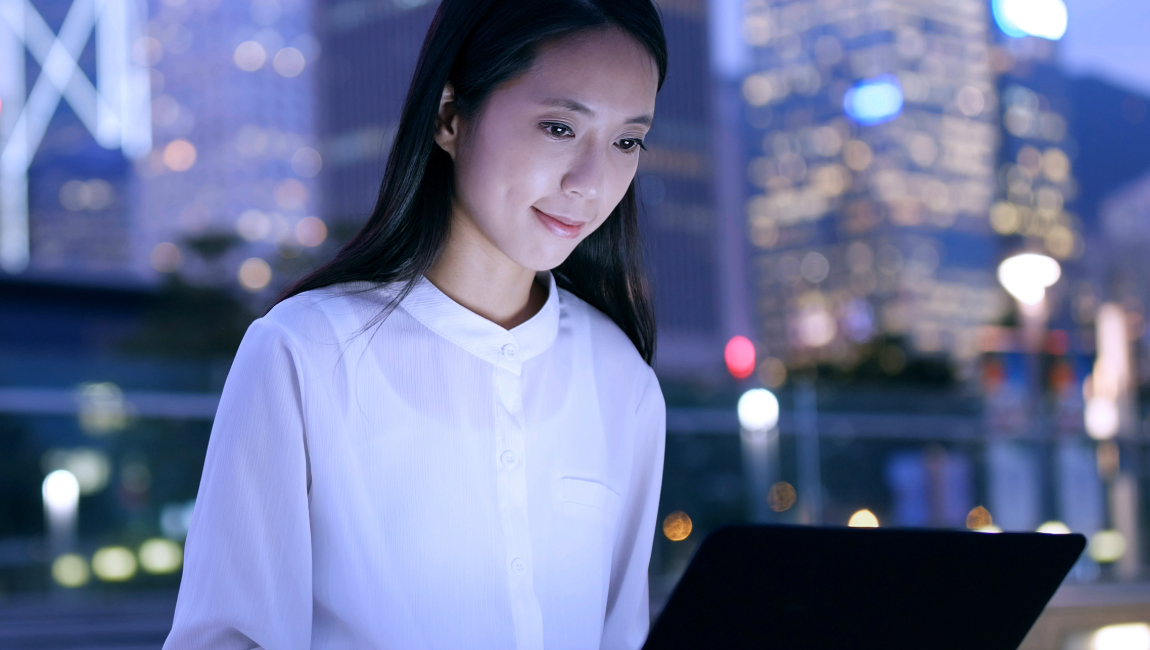 Woman sitting outside skyscrapers in evening while looking at laptop