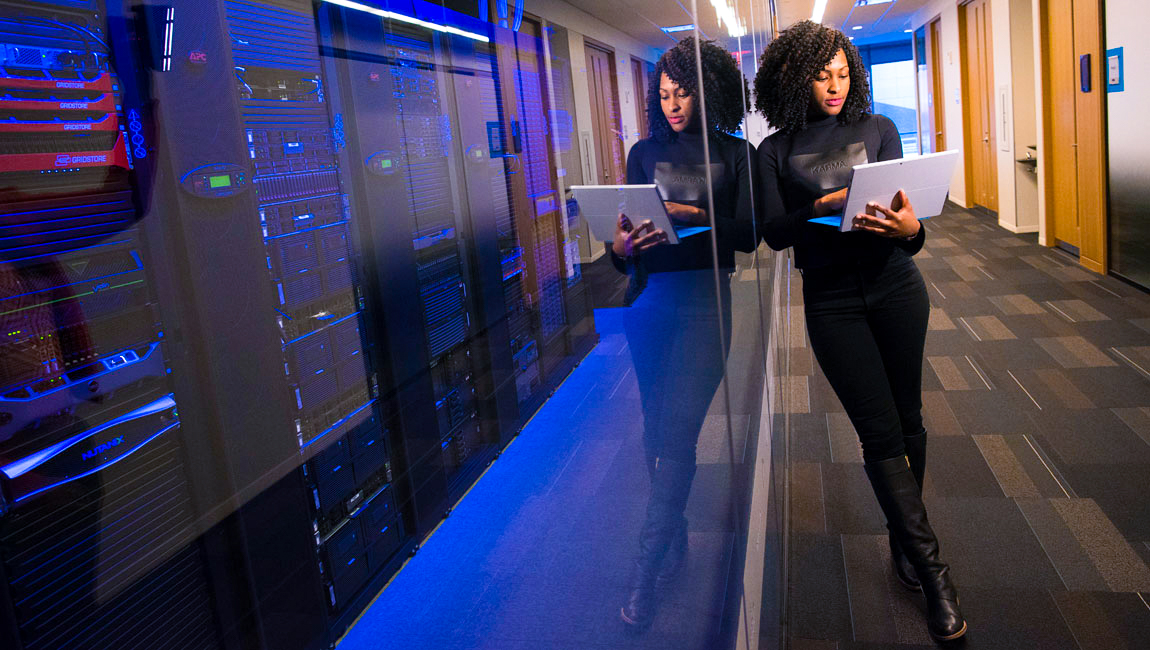 Businesswoman holding laptop while leaning against windows to server room