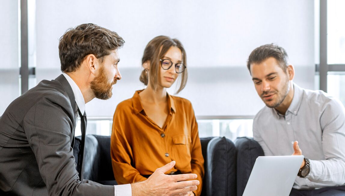 Three colleagues sat at a table discussing information on a laptop screen