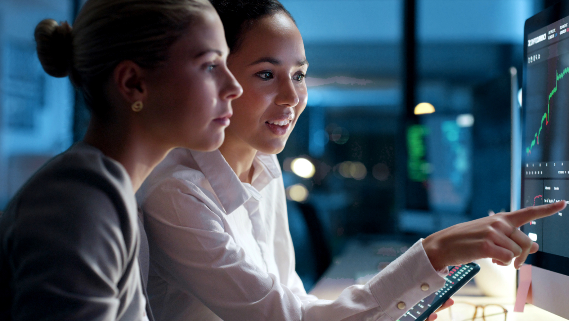 Two female colleagues pointing at desktop computer screen