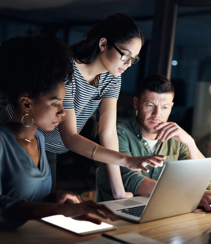 Three colleagues huddled around laptop in an office working late at night